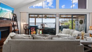 A modern living room with a large TV, a fireplace, and a view of the sea. - Karaoke,Arcade,Firepit,PrivateDock,Projector,Kayaks,SUP,Fishing,Massage,Mixology (Montgomery)