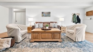 Un soggiorno con un ampio tavolino in legno, due poltrone beige, un tappeto decorato e un quadro appeso al muro.