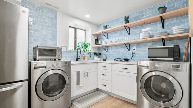 Una cucina moderna con elettrodomestici in acciaio inossidabile, mobili bianchi e backsplash in piastrelle blu.