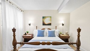 Un letto rifatto con cura, con testiera in legno, due comodini con lampade, un’opera d’arte appesa al muro e una finestra con tende bianche.