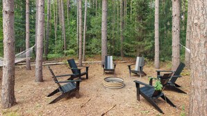Un entorno boscoso con una fogata rodeada de sillas Adirondack.