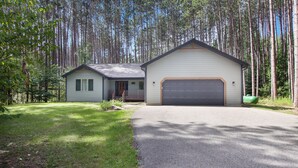 Una casa de dos pisos con garaje, rodeada de bosque.