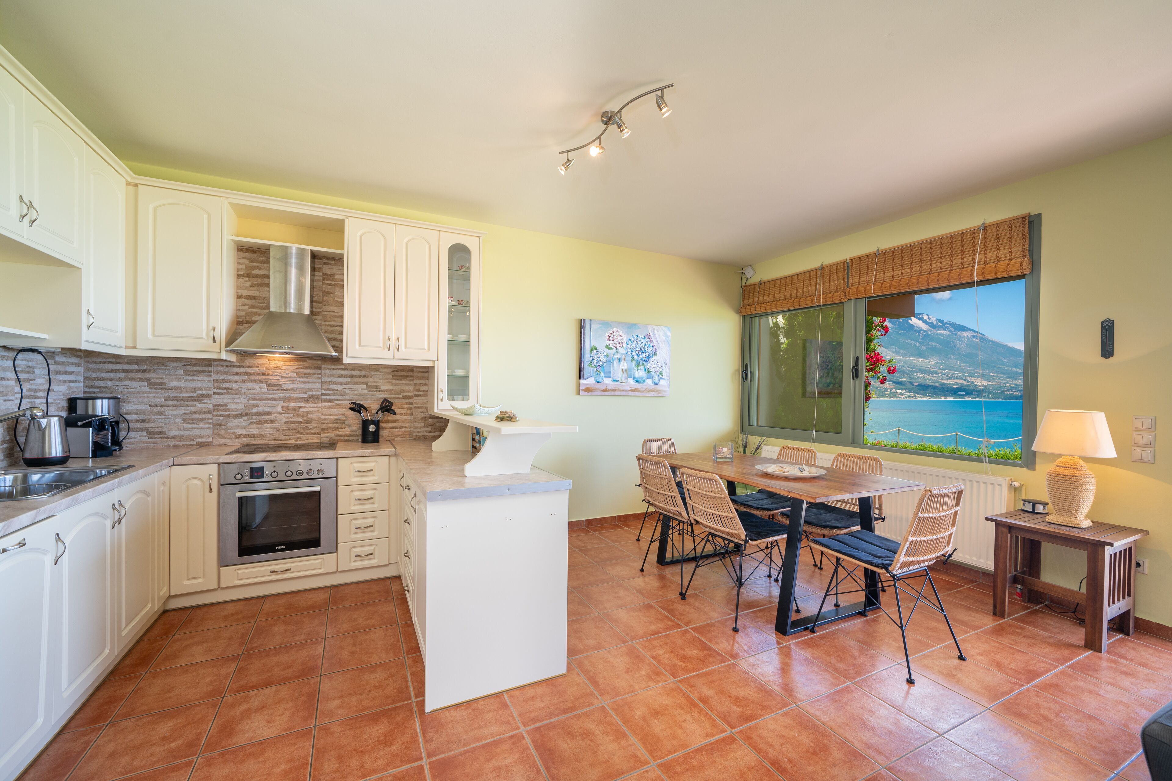 A modern kitchen with white cabinets, a built-in oven, and a dining area with a table and chairs.