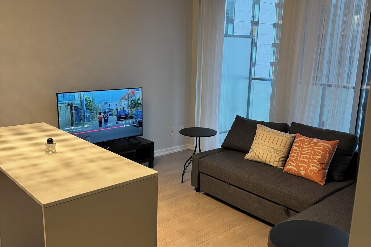 Ein modernes Wohnzimmer mit einer Couch, einem kleinen Couchtisch, einem Fernseher und einem dekorativen Kronleuchter.