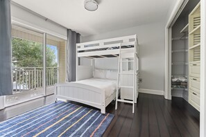 Quarto com beliche, uma janela grande com vista para árvores e um armário com prateleiras.