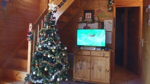Interno di una baita in legno con un albero di Natale addobbato, una televisione su un mobiletto in legno e una scala con un cartello.