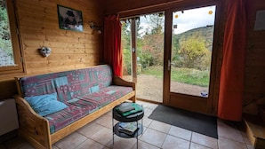 Interno di una baita in legno con un divano, un tavolino e vista su un paesaggio boschivo attraverso una porta in vetro.