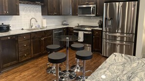 Una cucina moderna con mobili in legno scuro, elettrodomestici in acciaio inox, un piano di lavoro in granito e tre sgabelli neri.
