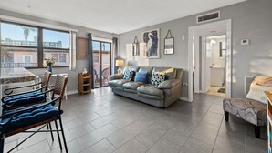 Una sala de estar moderna con un sofá gris, un comedor con una mesa de mármol y grandes ventanales que ofrecen vistas de la ciudad.