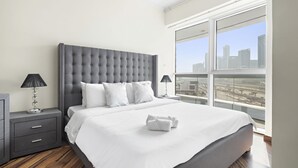 A modern hotel room with a large bed, a city view, and a grey upholstered headboard. - Spacious 2 BD in JLT with Marina Views (Dubai)