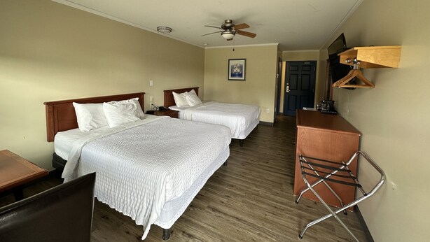 Habitación de hotel con dos camas, un escritorio, una silla, un ventilador de techo y un aparador de madera.