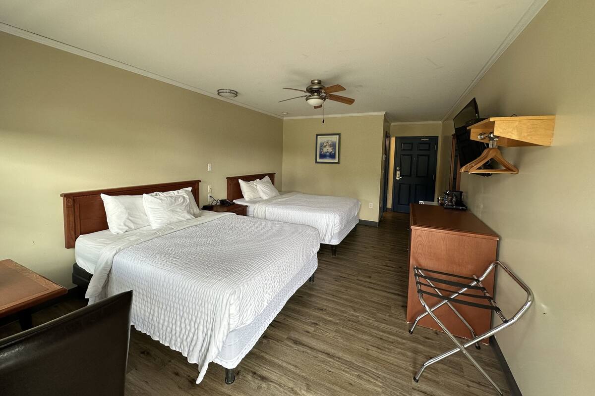 A hotel room with two beds, a desk, a chair, a ceiling fan, and a wooden dresser.