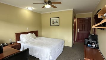 Une chambre d’hôtel équipée d’un lit, d’un bureau, d’une chaise, d’un ventilateur de plafond, d’une porte et d’une petite kitchenette.