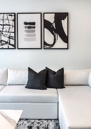 Uma sala de estar moderna com um sofá branco, almofadas pretas e três obras de arte abstratas em preto e branco na parede.