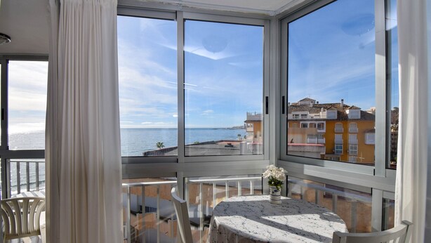 Un balcón con mesa y sillas, con vistas a la costa, edificios y el mar.