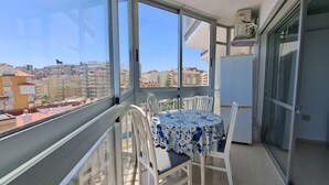 Un balcón con mesa y sillas, un refrigerador y vista a la ciudad.