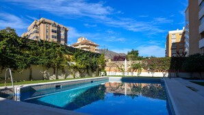 Una piscina con agua cristalina azul, rodeada de vegetación y edificios.