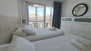Una habitación de hotel con una cama, una silla, un aparador y vistas a edificios a través de una ventana.