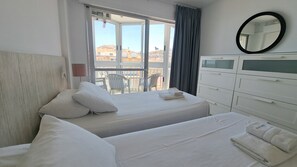 Une chambre dâhĂŽtel avec un lit, une chaise, une commode et une vue sur les bĂątiments, visible par la fenĂȘtre.