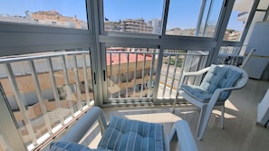 Un balcon donnant sur des immeubles, une chaise blanche et une table.