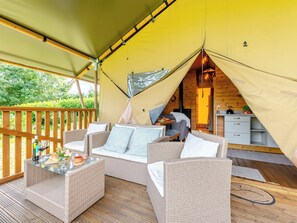 A cozy tented accommodation with wicker furniture, a dining area, and a view of the outdoors.