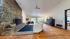 Un salón espacioso con chimenea de piedra, un sofá blanco, una mesa de centro y un piano.