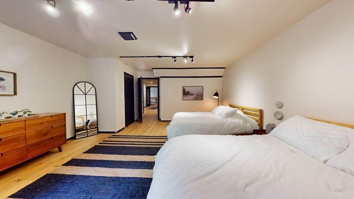 Habitación de hotel moderna con dos camas, un tocador de madera, un espejo y vista al pasillo.