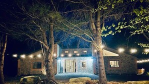Een stenen huis met een stenen dak, omringd door bomen en een houten wagen.