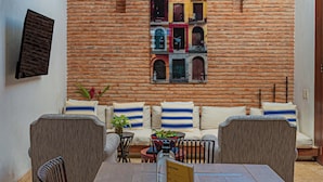A cozy seating area with a brick wall, a window with multiple panes, and a small table with a bottle. - Wynwood Casa Santisimo in Cartagena (Cartagena)