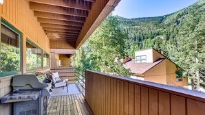 A wooden deck with a grill and outdoor furniture, overlooking a forested mountain area. - East Vail Condo w/ Pool, Hot Tub, & Free Bus Stop (Vail)