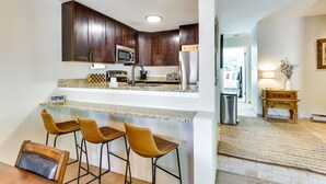 A modern kitchen with dark wooden cabinets, a microwave, and a refrigerator. There are three bar stools and a granite countertop. - East Vail Condo w/ Pool, Hot Tub, & Free Bus Stop (Vail)
