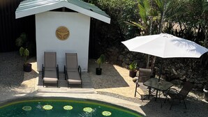 A swimming pool with clear water, surrounded by lounge chairs and a small building with a circular emblem. - Hotel Luz de Luna Bahia Ballena (Bahía Ballena)