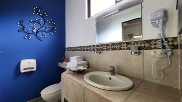 Un baño con pared azul, un lavabo con espejo arriba, un secador de pelo y un inodoro.