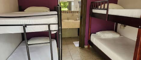 Habitación tipo dormitorio con literas, un baño pequeño con lavabo y espejo, y una ventana con vistas a zonas verdes.