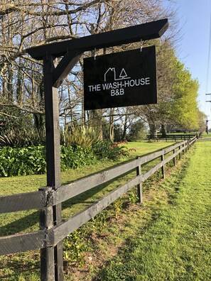Une enseigne indiquant « The Wash-House B&B », avec une clôture en bois et de la verdure en arrière-plan.