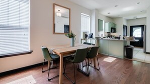 Une cuisine moderne dotée d’un îlot central, d’un coin repas avec une table et des chaises en bois, et d’une grande fenêtre avec des stores.