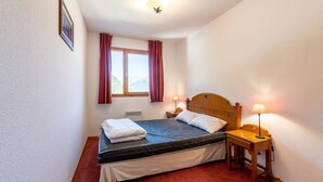 A single bed with a wooden headboard, two bedside lamps, a window with curtains, and a framed picture on the wall. - Apt 6 ppl near the ski runs (Modane)