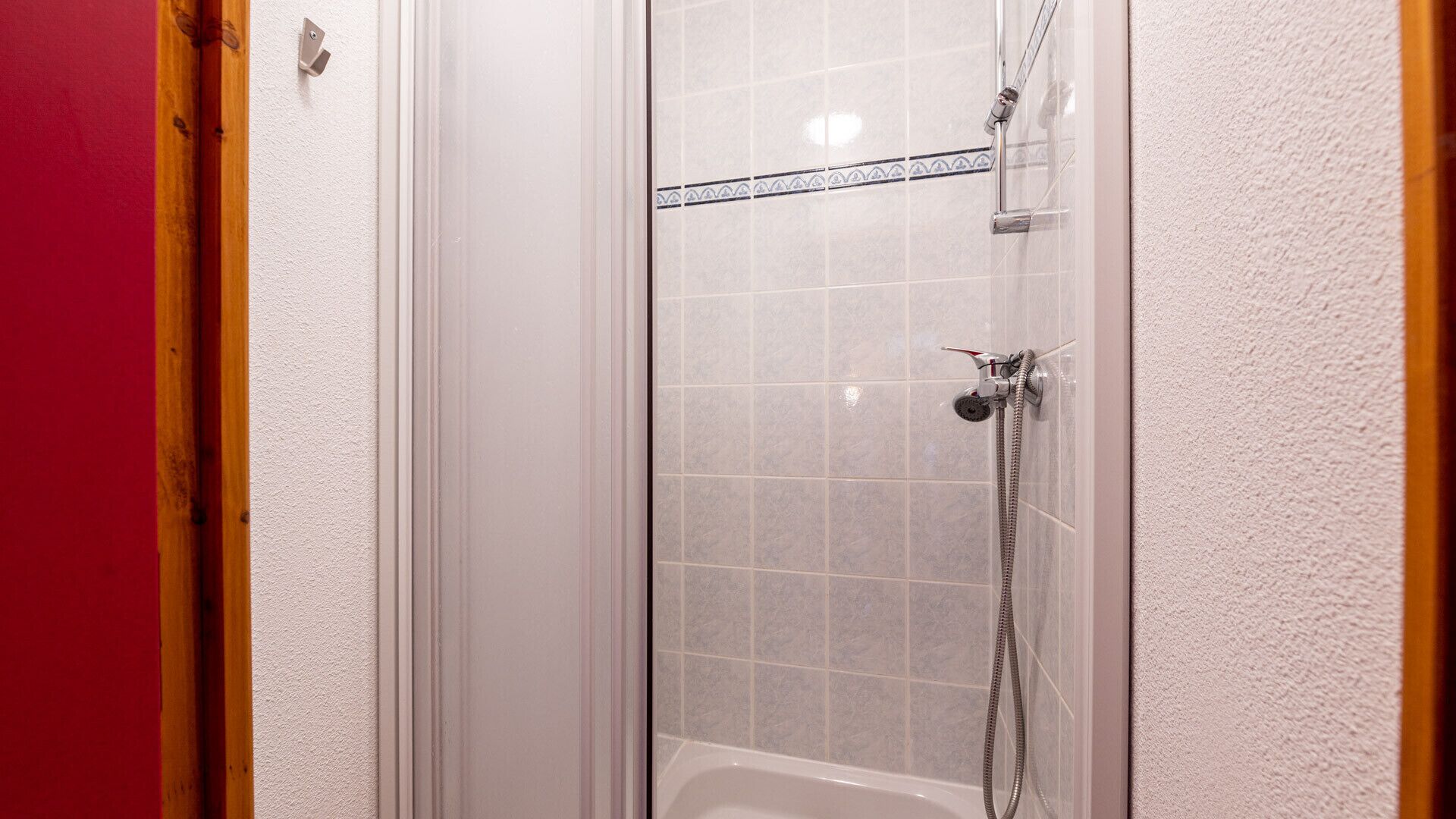 Una ducha con puerta de vidrio, un cabezal de ducha manual y un grifo empotrado en la pared.