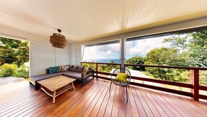 Un terrazzo in legno con un divano e una poltrona, affacciato su un paesaggio rigoglioso.