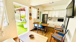 A compact kitchen with white cabinets, a microwave, and a refrigerator. There is a dining area with a wooden table and blue chairs. - Luxury 1 bed Apartment 6. Steps from the beach! (San Juan)