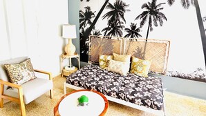 Una habitación con una cama, una silla, una mesita y un mural en la pared con palmeras.