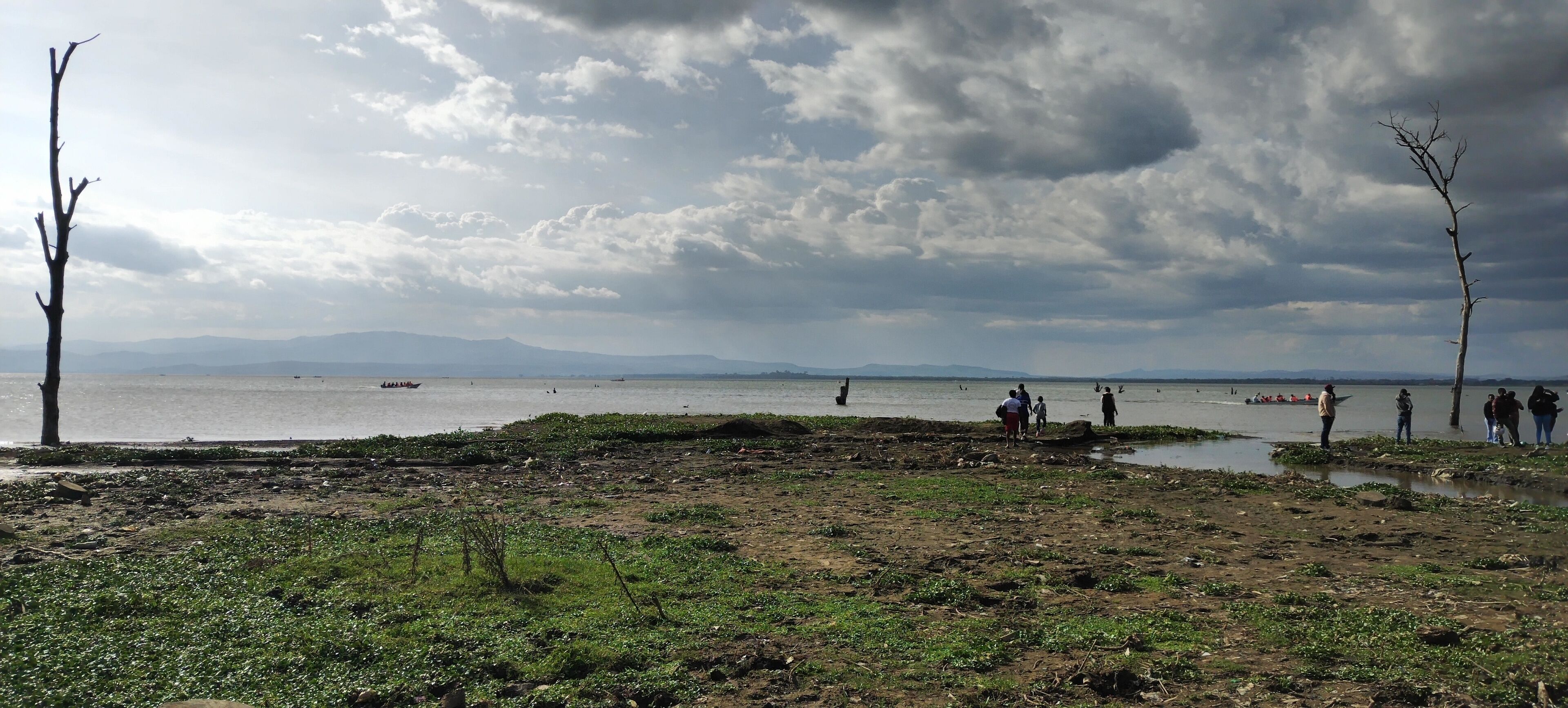 A beach with people, boats, and a cloudy sky.