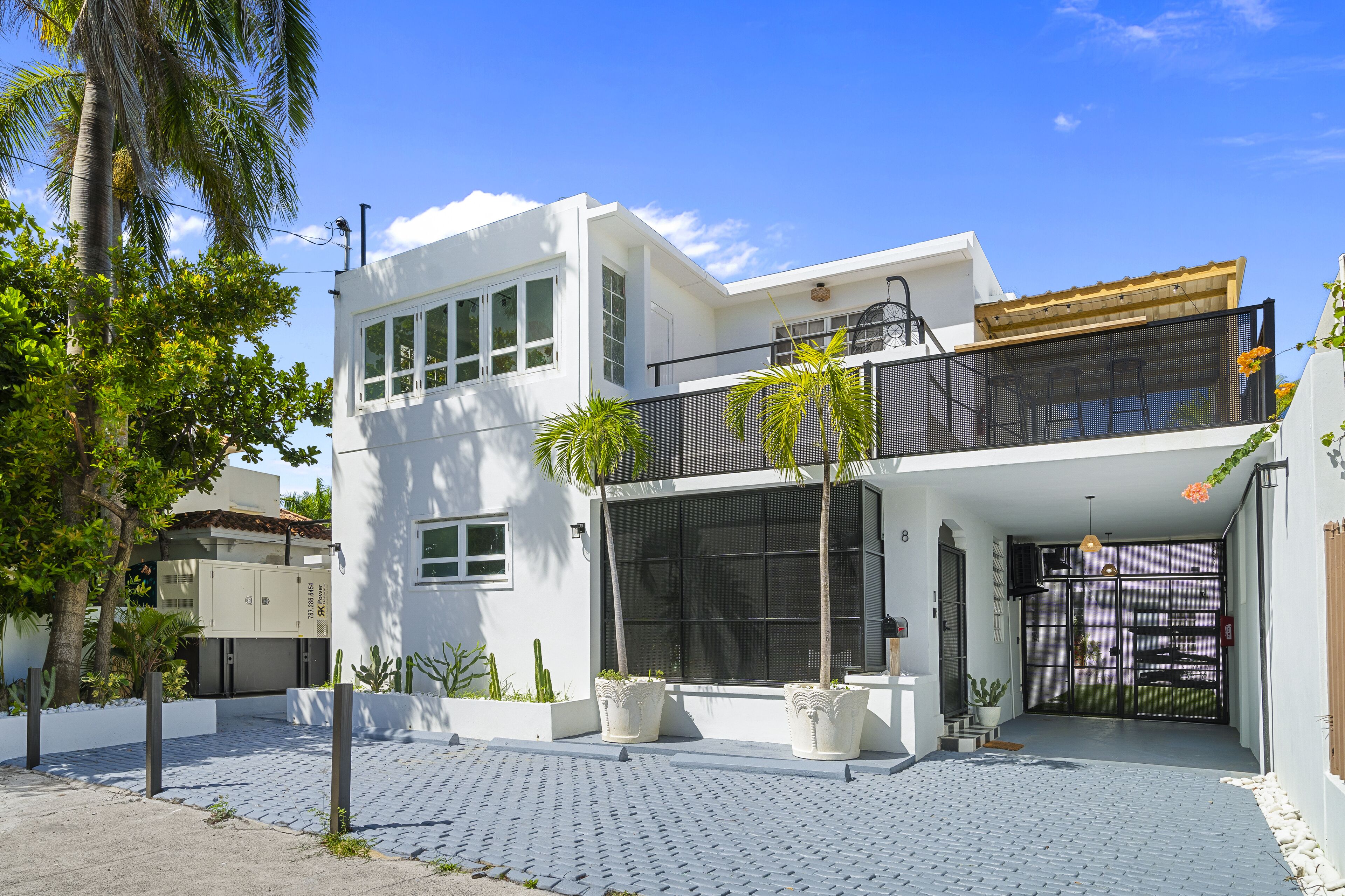 A modern two-story house with a balcony, large windows, and potted plants.