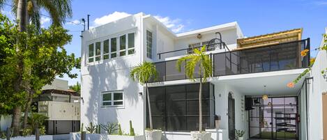 A modern two-story house with a balcony, large windows, and potted plants.