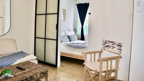 A room with a bed, a chair, a small table, and a sliding door leading to another room. - Luxury 1 bed Apartment 9. Steps from the beach! (San Juan)