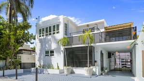 A modern two-story house with a balcony, large windows, and potted plants. - Luxury 1 bed Apartment 9. Steps from the beach! (San Juan)
