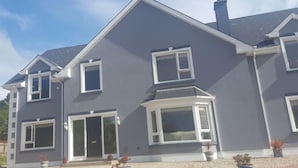 Een huis met twee verdiepingen, een grijze gevel, witte details en een schoorsteen.