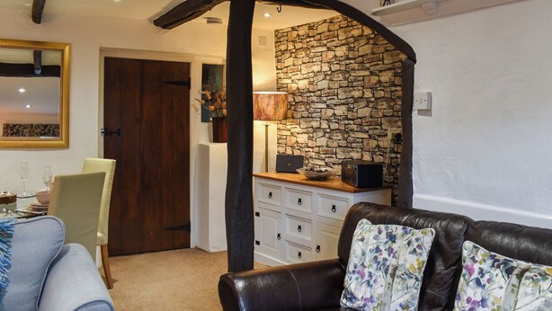 Um quarto com parede de pedra, porta de madeira, área de jantar com mesa e cadeiras e sofá de couro com almofadas florais.