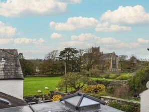 A view of a green field with sheep, a stone building with a tower, and a clear sky. - This quaint chocolate box cottage is nestled in the heart of Cartmel village. (Cartmel)