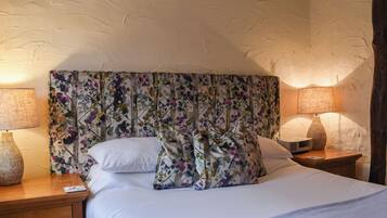 A bedroom with a floral headboard, two bedside lamps, a wooden nightstand, and a bed with white bedding.
